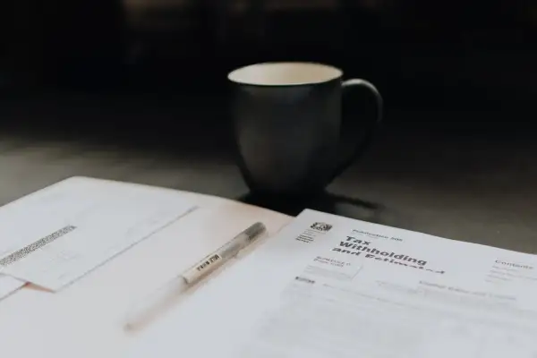 Kubek kawy i długopis leżą obok dokumentów podatkowych. Może to być duplikat faktury, który trzeba uzupełnić.