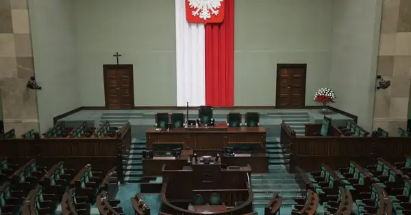 Pusta sala sejmowa, gotowa na głosowanie weta prezydenta. Biało-czerwona flaga i godło Polski na ścianie.